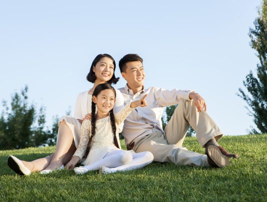 Cheerful Chinese family sitting on the lawn in a park