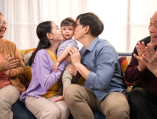 Happy multi-generational Asian family enjoying quality time together at home, cheering and smiling with a toddler